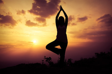 Woman training yoga on the mountain at sunset