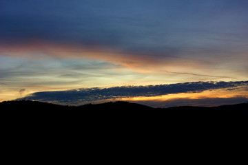 Landscape with forest and silhouettes of trees at sunset between clouds