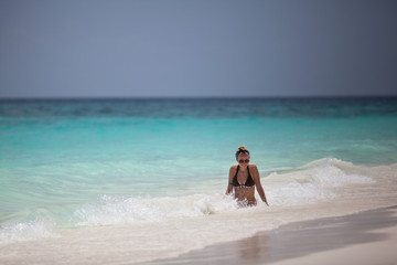 beautiful girl in sunglasses and in a dark swimsuit relaxing on the beach and enjoying the waves and warm water of Andaman sea/turquoise color of water and blue sky in the background/ turquoise color