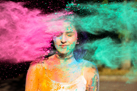 Beautiful brunette woman posing with exploding pink and green Holi powder around her