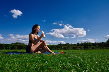 Girl sits in Park on a grass and holding a bottle of water.