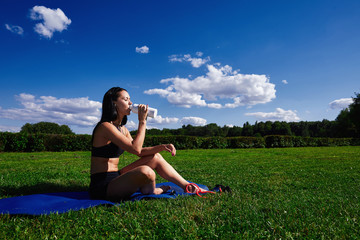 Girl sits in Park on the grass on a Sunny day and drinking water.