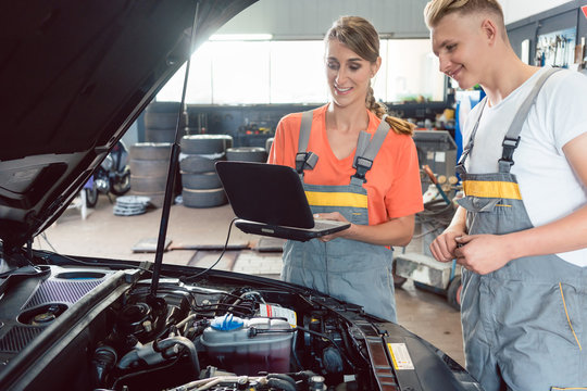 Experienced female auto mechanic checking the engine error codes scanned by a car diagnostic software while standing next to a motivated apprentice