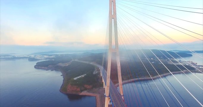 Flying high through clouds, aerial view of cable-stayed Russian Bridge across the Eastern Bosphorus strait and Russian island in Vladivostok, Russia. Early morning. Sunrise