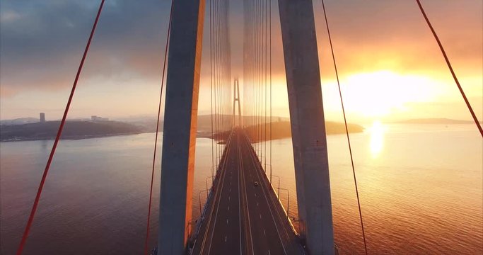 Flying above the road and between cables of cable-stayed Russian bridge across the Eastern Bosphorus strait on the way to Russian island in Vladivostok. Amazing sunrise. Aerial