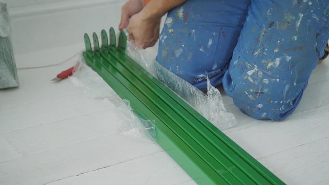 Male repairman unpacks green metal structures from polyethylene. On floor man opens five packages from packaging to assemble frame.
