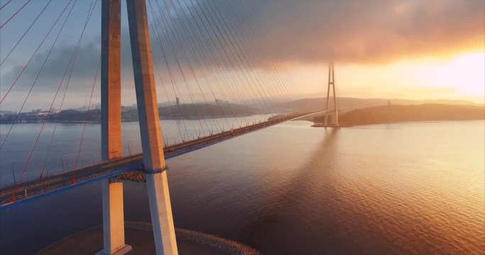 Flying backwards, aerial ascending view of cable-stayed Russian bridge across the Eastern Bosphorus strait on the way to Russian island in Vladivostok, Russia. Morning, sunrise