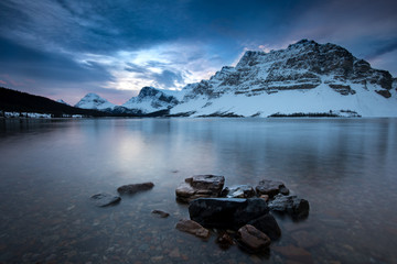 A calm lake surrounded by snowy mountains at dawn