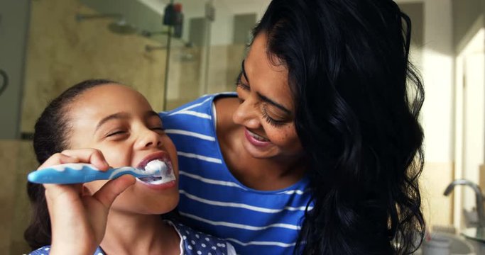 Mother teaching her daughter to brush her teeth in bathroom 