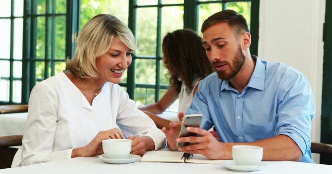 Male and female executives discussing over mobile phone 