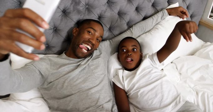 African American father and son taking selfie with mobile phone in bedroom 