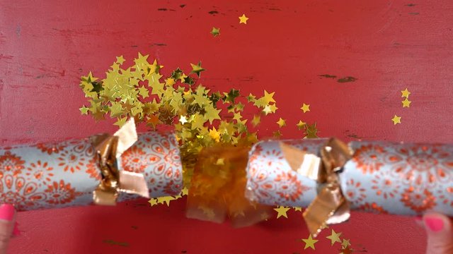 Festive surprise concept, opening a Christmas cracker bon bon with gold glitter stars on rustic red wood table