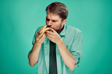 Man with a beard on a green background eating a hamburger, portrait, fast food