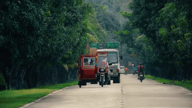 Telephoto lens shot of bikes and cars driving on small road in tropical island