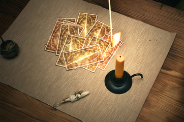 Tarot cards on fortune teller desk table. Future reading. Woman lights a candle by matches.