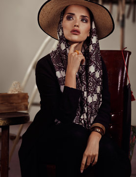 Model with a big scarf and hat sitting on a chair in a Mexican style in studio