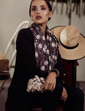 Model with a big scarf and hat sitting on a chair in a Mexican style in studio