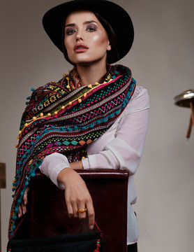 Model with a colourful scarf and big hat sitting on a flipped chair in a Mexican style in studio