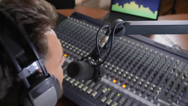 close-up DJ with headphones on his head works near mixer and speaks in microphone at recording studio
