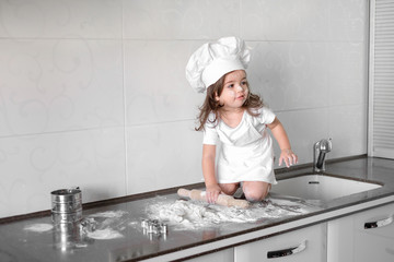 Little girl makes dough on kitchen with rolling pin