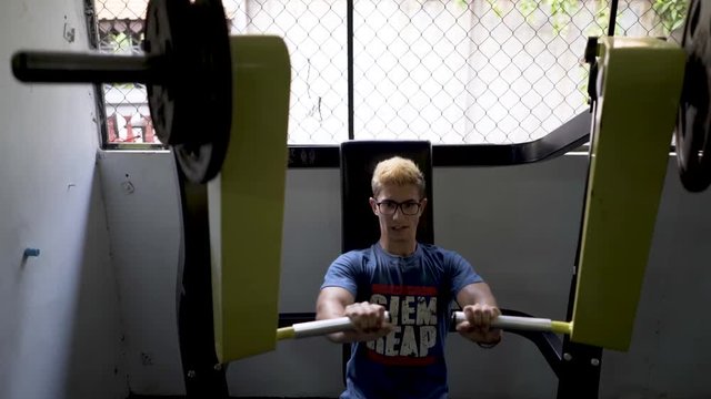 Teen bodybuilder pressing large weights on a universal machine in a gym.