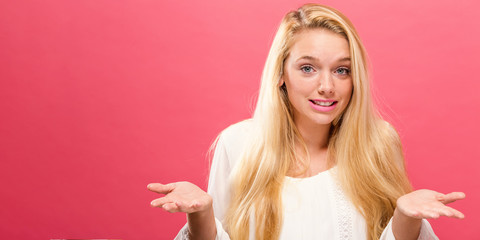 Young woman shrugging on a solid background