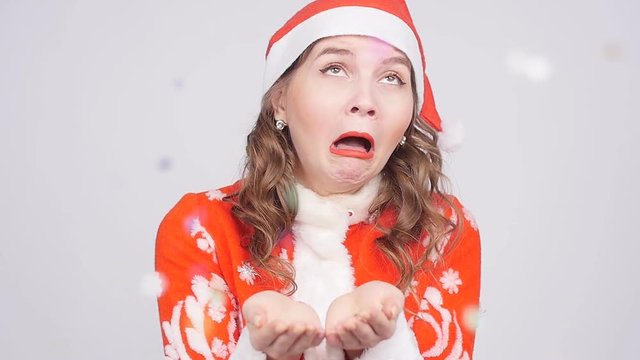 A funny young woman in Santa Claus hat sneezes at confetti