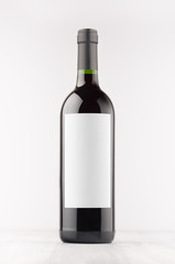 Dark wine bottle with blank white label on white wooden board, mock up, vertical. Template for advertising, design, branding identity.