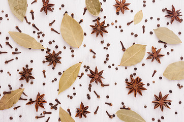 Anise stars, clove, bay leaves pattern on white wood background.