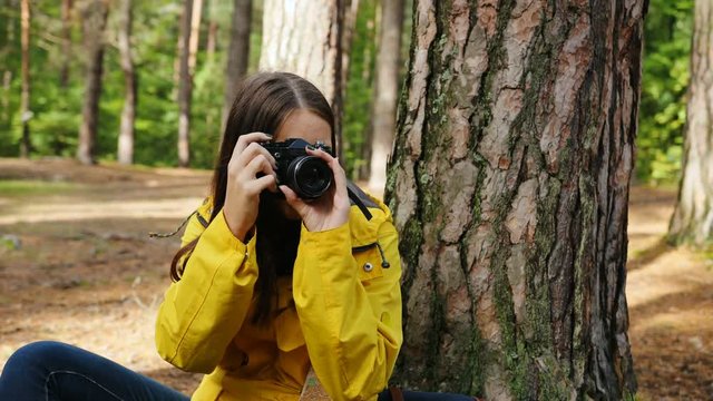Close up of the young charming woman sitting on the ground and taking photos of the nature on the vintage camera in the green forest around her. Outside. Portrait shot