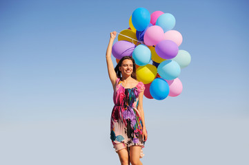 Beautiful, cheerful young woman in a bright dress with colorful balloons  on a field with a blue...
