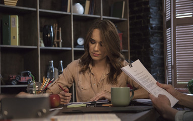 Young business woman sitting behind desk holding pencil and reading document