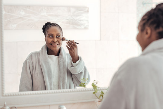 African Woman Applying Foundation To Her Cheek In The Bathroom