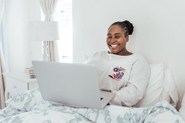 Smiling young African woman using a laptop in her bed