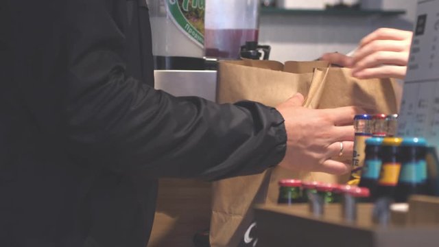 Hands putting burgers into bag. Man buys packaged food in cafe. 3840x2160