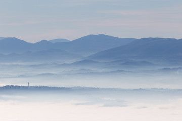 Fog filling Umbria valley, with layers of mountains and hills and various shades of blue, and Montefalco town silhouette in the foreground