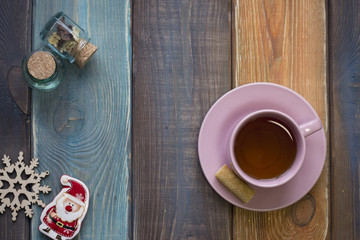Christmas still life with pink tea cup,saucer, tiny jars with corks, toy snowman and wooden snowflake on a colored wooden background, top view