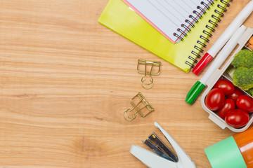 Office desk with supplies and lunch box with vegetables and almond. Top view with space for your text