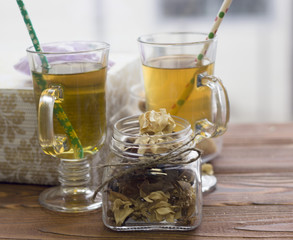 A festive still life with a decorative glass jar of dry flowers and two cups of fresh green tea with christmas patterned straws, light background