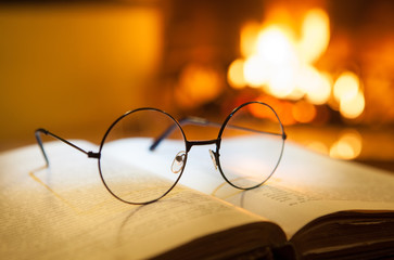 An open antique book and vintage glasses in front of the fireplace. Evening fairy tales. Fantasy.