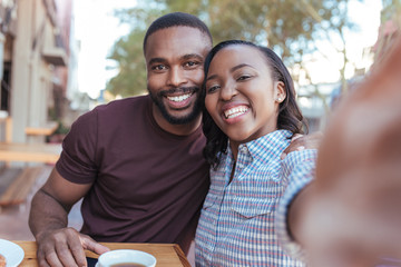 Smiling young African couple taking selfies together at a cafe