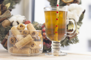 A bright morning with a glass clear cup of green tea, bowl of cookies and a pine wreath, a light background