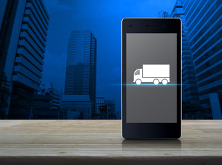 Truck flat icon on modern smart phone screen on wooden table over office city tower, Business transportation service concept