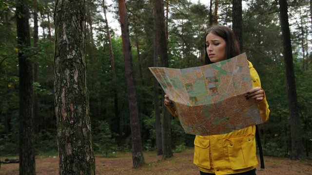 Young beautiful woman in yellow coat getting lost in the forest. She looking for the route with a help of a map. Outside