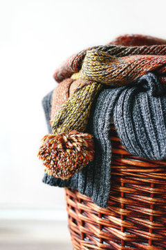Stack of knitted winter scarfs on straw basket isolated on white background.