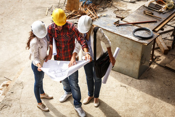 Two female  architects discuss with head engineer about blueprints of construction site.