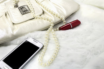 Women's clutch, lipstick, necklace, phone on white fur.
