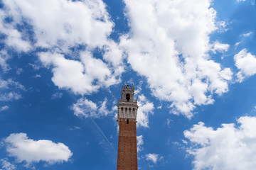 Fototapeta na wymiar Detail of the Torre del Mangia 87 m. (Tower of Mangia) on blue sky with clouds. Siena, Italy