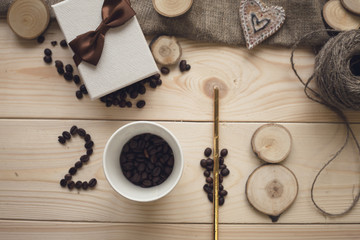 2018 inscription of cup of coffee beans and wooden slices with a gift box and skein of threads on a light wooden background, top view