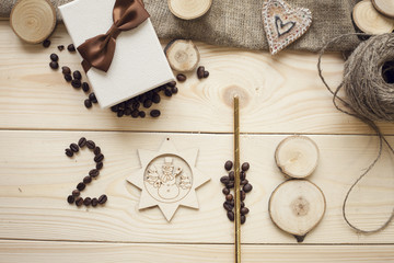 2018 inscription of coffee beans, wooden star and wooden slices with a gift box and skein of threads on a light wooden background, top view